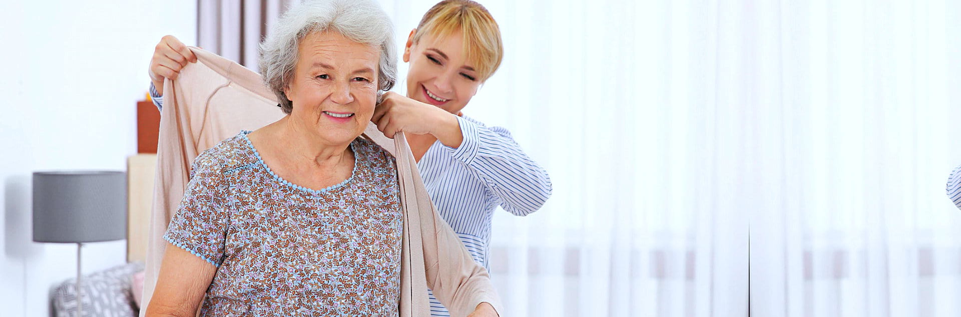 portrait of caregiver helping senior woman in dressing